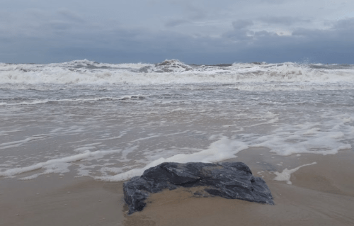 A rocky shore with waves crashing against the beach under a cloudy sky.