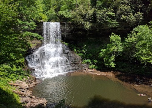 A serene waterfall cascades into a tranquil pool, surrounded by lush green trees and rocky terrain.