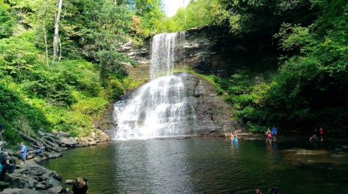 A scenic waterfall cascades into a serene pool, surrounded by lush greenery and people enjoying the natural beauty.