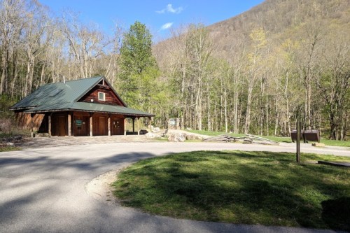 A rustic building with a green roof surrounded by trees and a gravel path in a serene outdoor setting.