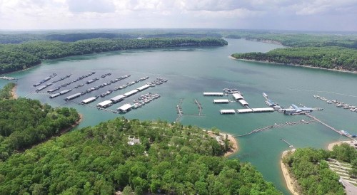 Aerial view of a serene lake surrounded by green trees, featuring several boat docks and marinas.