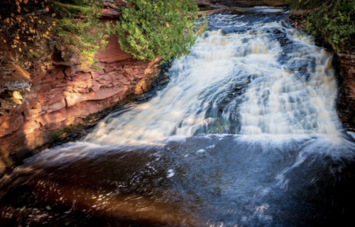 A serene waterfall cascading over rocky terrain, surrounded by lush greenery and flowing into a calm river below.