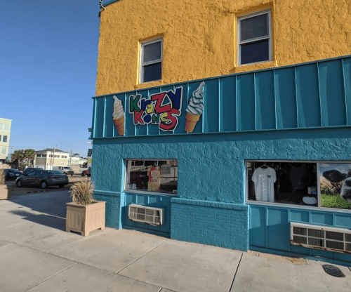 Colorful storefront of "Krazy Kones" ice cream shop with bright yellow and blue walls. Windows display merchandise.