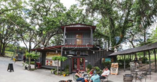 A rustic building surrounded by trees, with people sitting outside and enjoying the outdoor space.