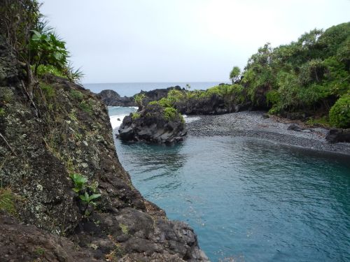 A serene coastal scene featuring rocky shores, lush greenery, and calm blue waters under a cloudy sky.