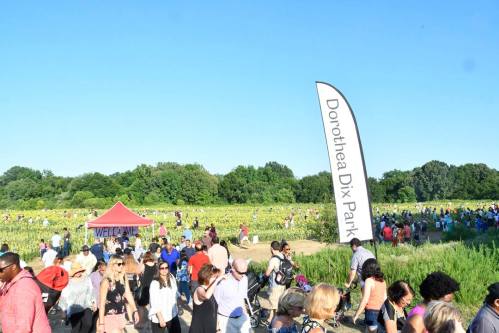 Crowd of people at Dorothea Dix Park, with a welcome tent and a large flag in a sunny outdoor setting.