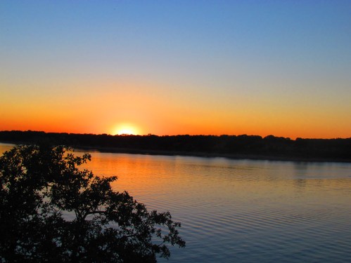 A serene sunset over a calm river, with vibrant orange and blue hues reflecting on the water's surface.