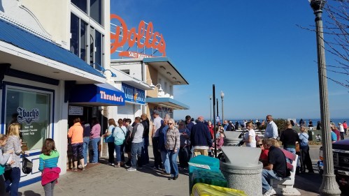 Crowd of people waiting outside Dolly's Salt Water Taffy shop on a sunny day by the beach.