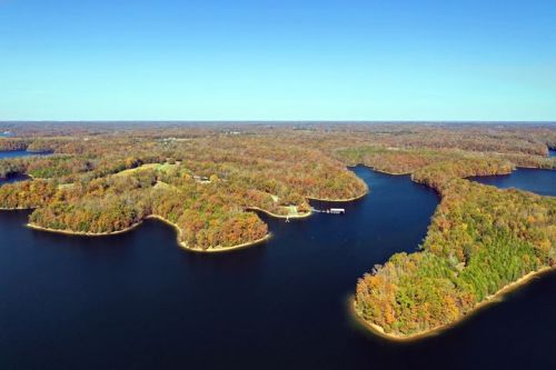 Aerial view of a serene lake surrounded by colorful autumn foliage and wooded islands under a clear blue sky.