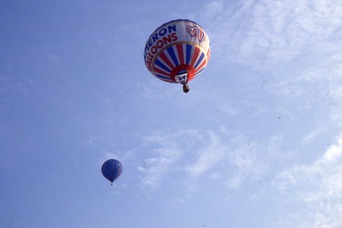 Two colorful hot air balloons float in a clear blue sky with wispy clouds.