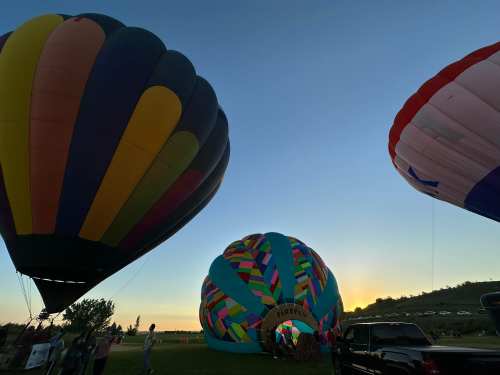 Colorful hot air balloons at sunset, with people gathered near a balloon entrance labeled "Firefly."