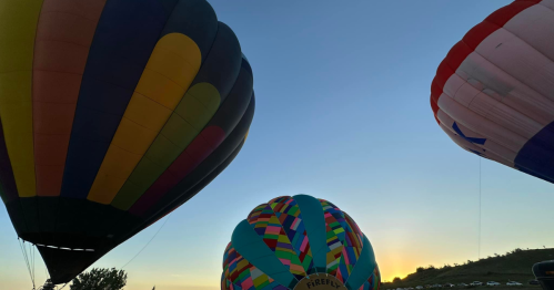 Colorful hot air balloons against a clear sky at sunset, with the sun peeking in the background.
