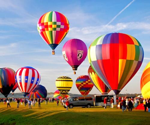 A vibrant scene of colorful hot air balloons in the sky above a crowd at a festival on a sunny day.