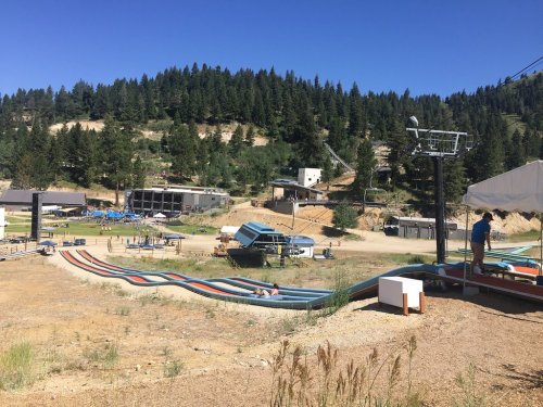 A summer water slide park with colorful slides, surrounded by trees and hills under a clear blue sky.