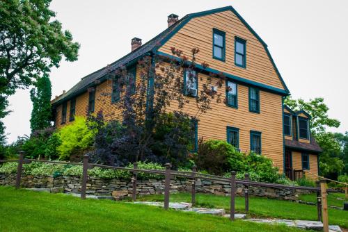 A large, two-story yellow house with blue trim, surrounded by greenery and a stone wall in a tranquil setting.