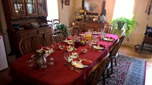 A beautifully set dining table with red tablecloth, plates, glasses, and a centerpiece, ready for a meal.