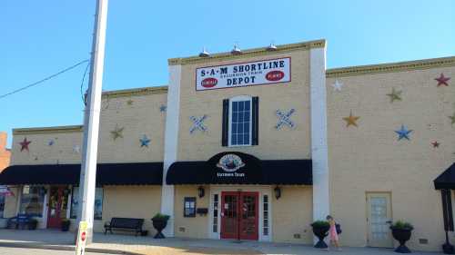 Historic building with a sign reading "S-A-M Shortline Depot," featuring decorative stars and a black awning.