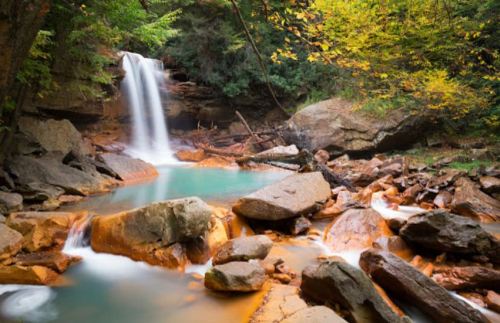 A serene waterfall cascades into a turquoise pool, surrounded by lush greenery and rocky terrain.