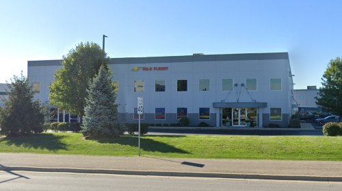 A modern commercial building with a landscaped front, featuring large windows and a clear blue sky.