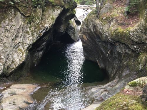 A serene natural scene featuring a rocky gorge with dark water flowing through, surrounded by moss-covered stones.