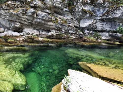 Clear green water flows over smooth rocks, surrounded by rugged cliffs and lush vegetation.