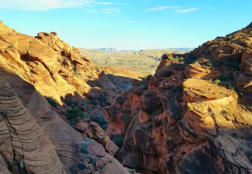 A scenic view of rugged, orange rock formations and a canyon under a clear blue sky.