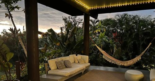 Cozy outdoor seating area with a hammock, surrounded by lush greenery and a sunset sky.