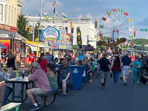 A bustling street fair with food stalls, a ferris wheel, and crowds of people enjoying the festivities.