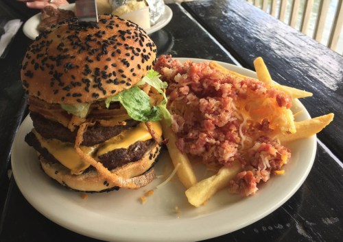 A large burger with two patties, cheese, lettuce, and crispy onions, served with fries and a side of coleslaw.