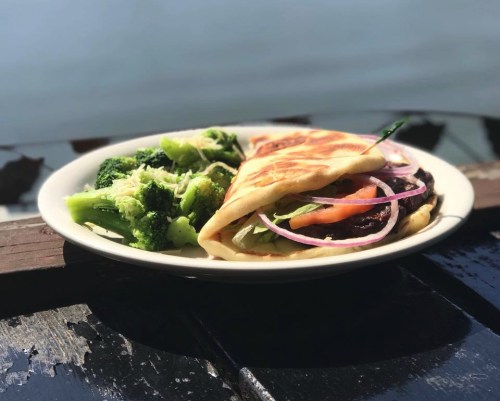 A plate with a folded flatbread filled with vegetables and a side of steamed broccoli.