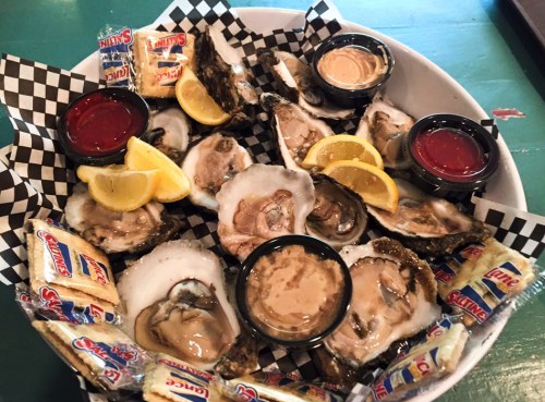 A platter of fresh oysters on the half shell, served with lemon wedges, cocktail sauce, and crackers.