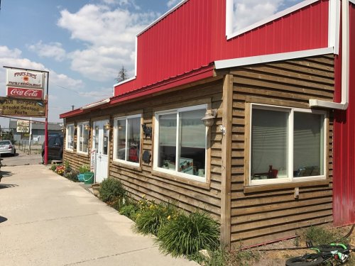 A rustic wooden building with a red roof, featuring large windows and a sign for a restaurant.