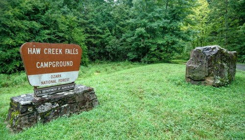 Sign for Haw Creek Falls Campground in Ozark National Forest, surrounded by lush green grass and trees.
