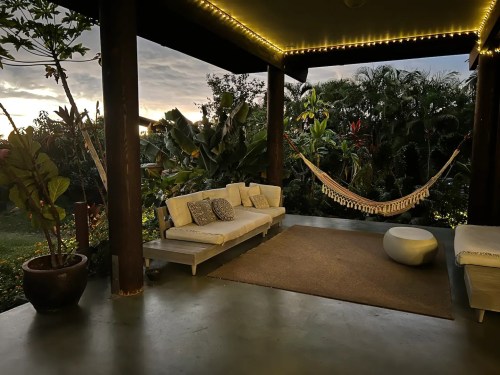 Cozy outdoor seating area with a hammock, surrounded by lush greenery and soft evening light.