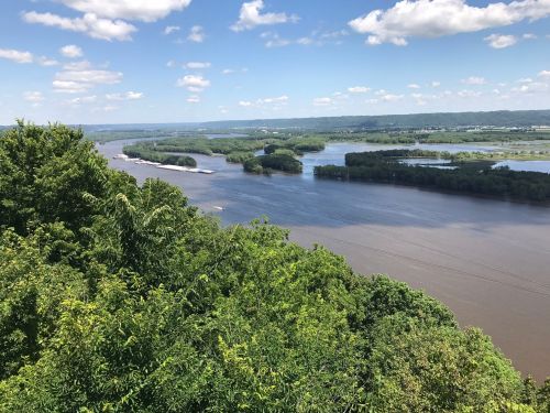 A scenic view of a river winding through lush green landscapes under a blue sky with fluffy clouds.