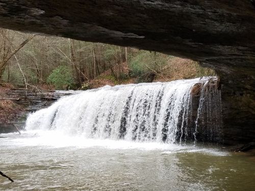 A serene waterfall cascades over rocks, framed by a natural stone arch and surrounded by lush greenery.