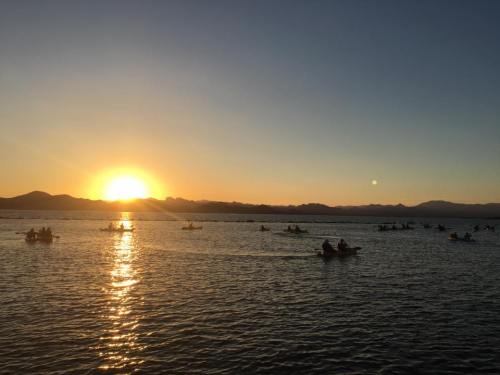 A serene sunset over a lake, with silhouettes of kayakers paddling in the water against a backdrop of mountains.