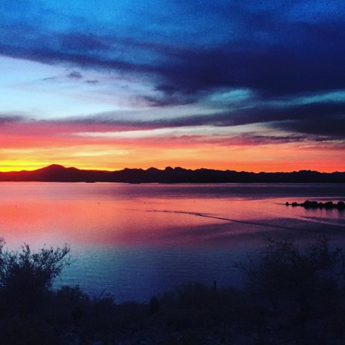 A serene sunset over a calm lake, with vibrant orange and purple hues reflecting on the water's surface.
