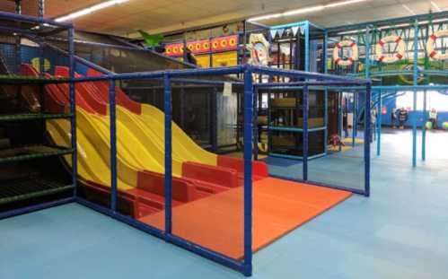 Colorful indoor playground featuring slides, climbing structures, and safety mats in a spacious play area.