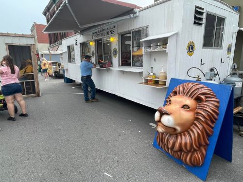 A food truck with a lion head decoration, serving customers at an outdoor event. People are gathered nearby.