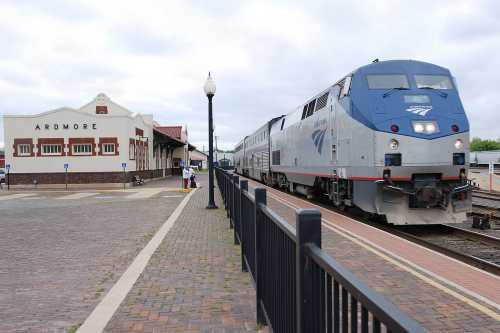 Amtrak train arriving at Ardmore station, with a historic building and passengers on the platform.