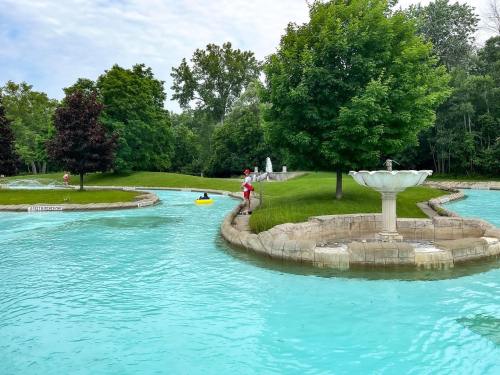 A serene water park scene with a lazy river, lush greenery, and a person in a red shirt near a fountain.