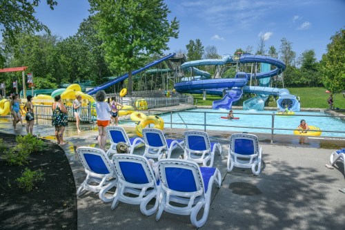A water park scene with slides, a pool, and people enjoying the attractions on a sunny day. Lounge chairs are in the foreground.