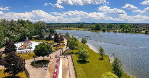 A scenic view of a water park beside a river, with slides, greenery, and people enjoying the sunny day.
