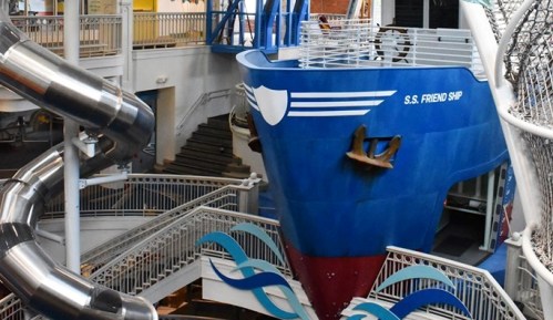 A large blue ship structure with a red bottom, part of an indoor water park, featuring slides and decorative waves.
