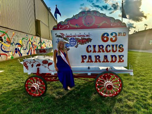 A woman in a blue gown sits on a colorful circus parade float, featuring "63rd Circus Parade" in bold letters.