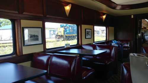 Interior of a vintage train car with red seating, tables, and a view of a blue locomotive outside the window.