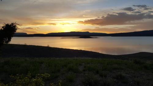 A serene sunset over a calm lake, with silhouettes of distant mountains and a grassy foreground.