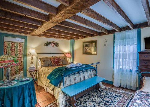 Cozy bedroom with wooden beams, a patterned bedspread, vintage decor, and a warm, inviting atmosphere.