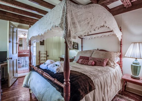 Cozy bedroom featuring a four-poster bed with a lace canopy, warm lighting, and rustic wooden beams.